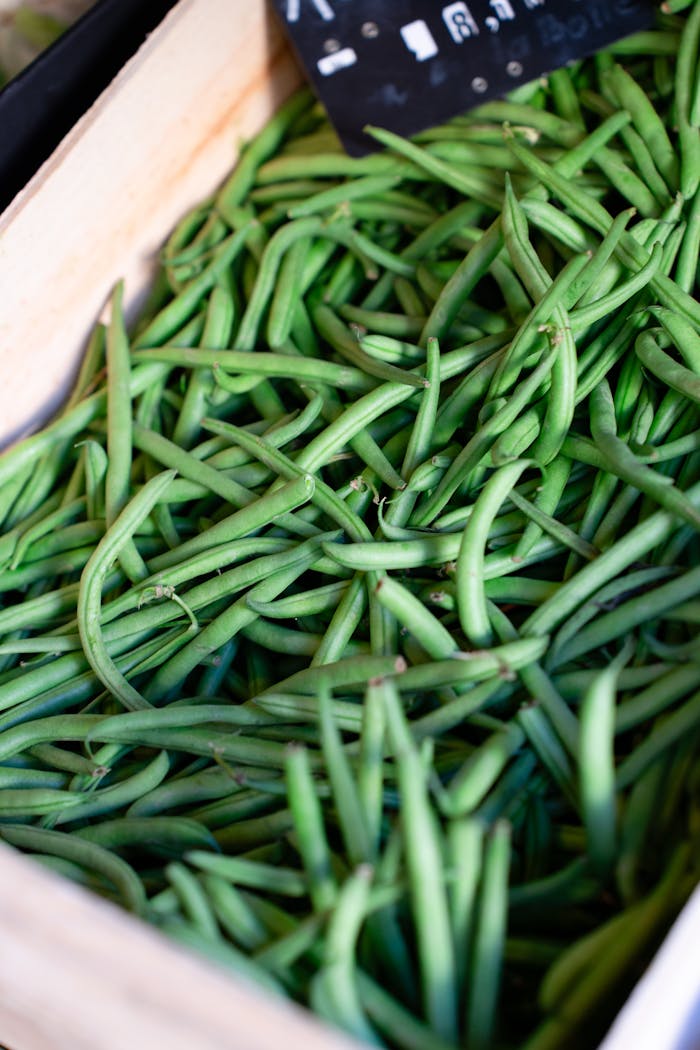 Close-up of fresh green beans displayed in a wooden crate at a local market.
